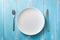 White Plate on blue wooden background with utensils