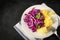 White plate of boiled potatoes with red cabbage salad on a towel on a black background, top view, lean vegetarian food