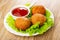 White plate with bowl of ketchup, small fried pies on leaves lettuce on wooden table