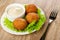 White plate with bowl of mayonnaise, round fried pies on lettuce, fork on wooden table