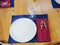 White plate with a crystal glass fork and knife on a blue napkin on a wooden light table. New shiny cutlery. Closeup