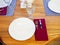 A white plate with a crystal glass and silver cutlery in a red napkin on the table. Cafe table setting. Closeup photo