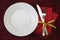 White plate with fork and knife on a red cloth napkin with a gold ribbon on a red tablecloth Holiday concept, Christmas, Valentine