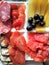 A white plate of four section cuts. Laid out pieces of meat of different types, cheese and olives.
