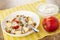 White plate with granola, yogurt, pieces of apple, bowl with yogurt, apple on napkin on wooden table