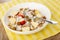 White plate with granola, yogurt, pieces of apple, spoon on napkin on wooden table