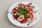 White plate of healthy classic delicious caprese salad with tomatoes and mozzarella cheese with basil leaves and strips of soy