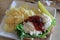 White plate on kitchen table, with open faced chicken salad, chips and pickle