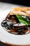 White plate with mussels decorated with a basil on a table in a restaurant . Different focus, close-up.