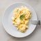 white plate with pan-fried scrambled eggs on white light background with tomatoes. Omelette, top view