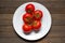 White plate with red ripened tomatoes on wooden table with copy space