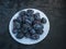 White plate with ripe prunes on a dark wooden background