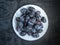 White plate with ripe prunes on a dark wooden background