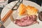 White plate with sliced, rare, roast beef, wedge of cheddar cheese, section of a bun and a cheese knife