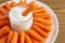 White plate with small peeled pieces of baby carrot and sauce on textured wooden table