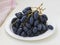 White plate with sweet and tasty long berry blue grapes on a table. Bunches of juicy ripe dark grapes. Close-up of delicious