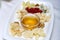 A white plate with various types of cheese, decorated with a sprig of red currant berries, nuts, served with a saucer of honey