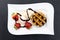 White plate with waffle, ice and strawberries decorated with chocolate stripes on a dark slate