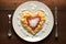 On a white plate with a wood background, heart shaped pasta is topped with tomato sauce and parmesan cheese
