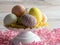 A white platter topped with string decorated Easter eggs and yellow paper shred sitting on a surface filled with pink paper shreds