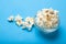 White popcorn in a glass bowl on a blue background