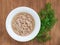 White porcelain bowl with shredded tuna in oil for cooking salad and green dill on a wooden background. Seafood, healthy eating