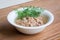 White porcelain bowl with shredded tuna in oil for a salad and green dill on a wooden background. Seafood, healthy eating and cook