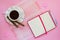 White porcelain cup with coffee, two coffee rolls on saucer with wavy edge and paper notebook with ball pen on a pink table napkin