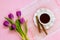 White porcelain cup with coffee, two sweet coffee rolls on saucer with wavy edge and and bouquet of pink or purple tulips