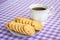 White porcelain cup with tea and sweet oatmeal cookies with pieces of dark chocolate on a white saucer on a white purple checkered