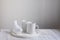 White porcelain cups and figurine of a bullfinch bird on a tray on wooden gray table