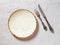 White porcelain dinner plate, vintage table knife and fork on a textured gray background. Empty speckled plate with brown border