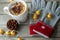 White porcelain mug filled with milk and corn flakes. Nearby are gray-red gloves with embroidered snowflake and metal Christmas