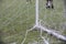 A white post of football goal with a white broken and messy net, while boy`s game playing on.