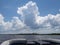 White puffy clouds blue sky from fantail of pontoon boat traveling up the intercoastal waterway with green shoreline