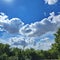 White Puffy Clouds, Deep Blue Sky and Green Trees in Foreground