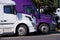 White and purple big rigs semi trucks stand on truck stop side b