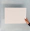 White rectangular blank sheet hold by a women`s hand in front of a blue background