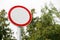 White with red border empty road round sign close up on blurred background of sky and trees