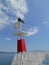 White and red metal lighthouse next to the sea, standing on dock