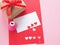 White and red paper, heart-shaped punches, red bow tie gift box and decorations for making a love card on a pink background.