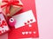 White and red paper, heart-shaped punches, red bow tie gift box and decorations for making a love card on a pink background.