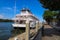 A white and red steamboat docked in the Savannah River surrounded by lush green trees with blue sky and clouds and a tall hotel