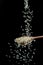 White rice grains falling down into the spoon at black background. Popular food and main ingredient of risotto and pilau