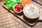 A white rice in wooden bowl and chopsticks with carrots, black sesame , and tomatoes vegetables on wooden board. Healthy food and