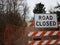 White road closed sign and striped barricade with trail or path