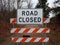 White road closed sign and striped barricade with trail or path