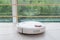 white robot vacuum cleaner vacuuming tiled floor, reflecting in panoramic window with fence. modern smart cleaning technology hous