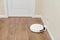 White robotic vacuum cleaner is charged from an electrical outlet on the base, wooden laminate