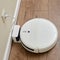 White robotic vacuum cleaner is charged from an electrical outlet on the base, wooden laminate